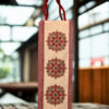 Canvas wine bottle bag with traditional red and green mandala designs and a maroon rope handle.
