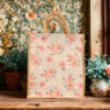A medium cream-colored jute bag featuring pink rose floral print and natural jute handles.
