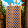 A medium-sized rectangular jute bag with a pattern of evenly spaced blue polka dots on a natural jute background.