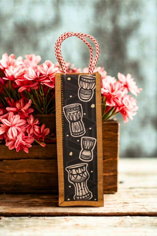Jute bottle bag with a black fabric panel featuring traditional djembe drum prints and sturdy red-and-white braided rope handles.