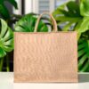 Plain juco bag with short handles placed upright on a display surface in a workshop or warehouse setting.