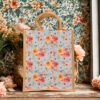 A medium jute bag with sky blue floral print featuring red and yellow roses