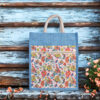 Blue jute bag featuring a colorful floral print and front zipper pocket with sturdy rope handles.