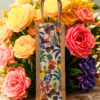 A tall, narrow jute bag with a colorful, whimsical print featuring tropical birds, flowers, and foliage.